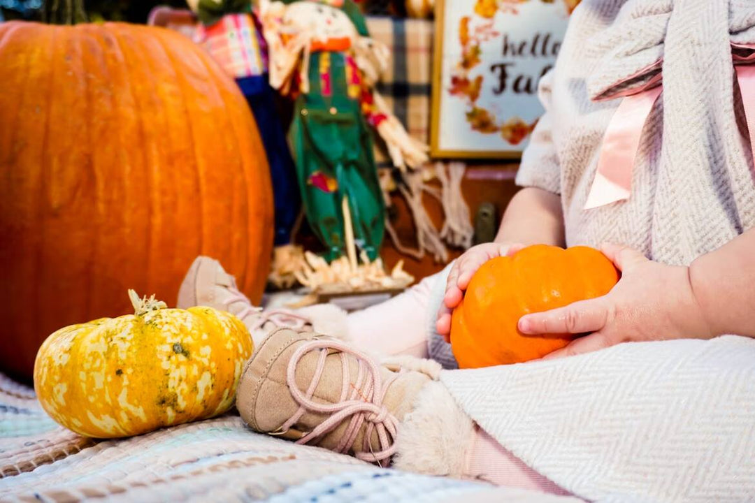 baby sitting on a blanket holding fall decorations