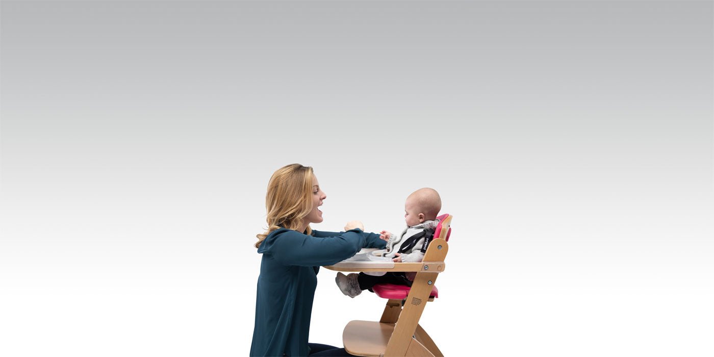 Mother talking to baby secured in a pink Beyond Junior Y High Chair from Abiie