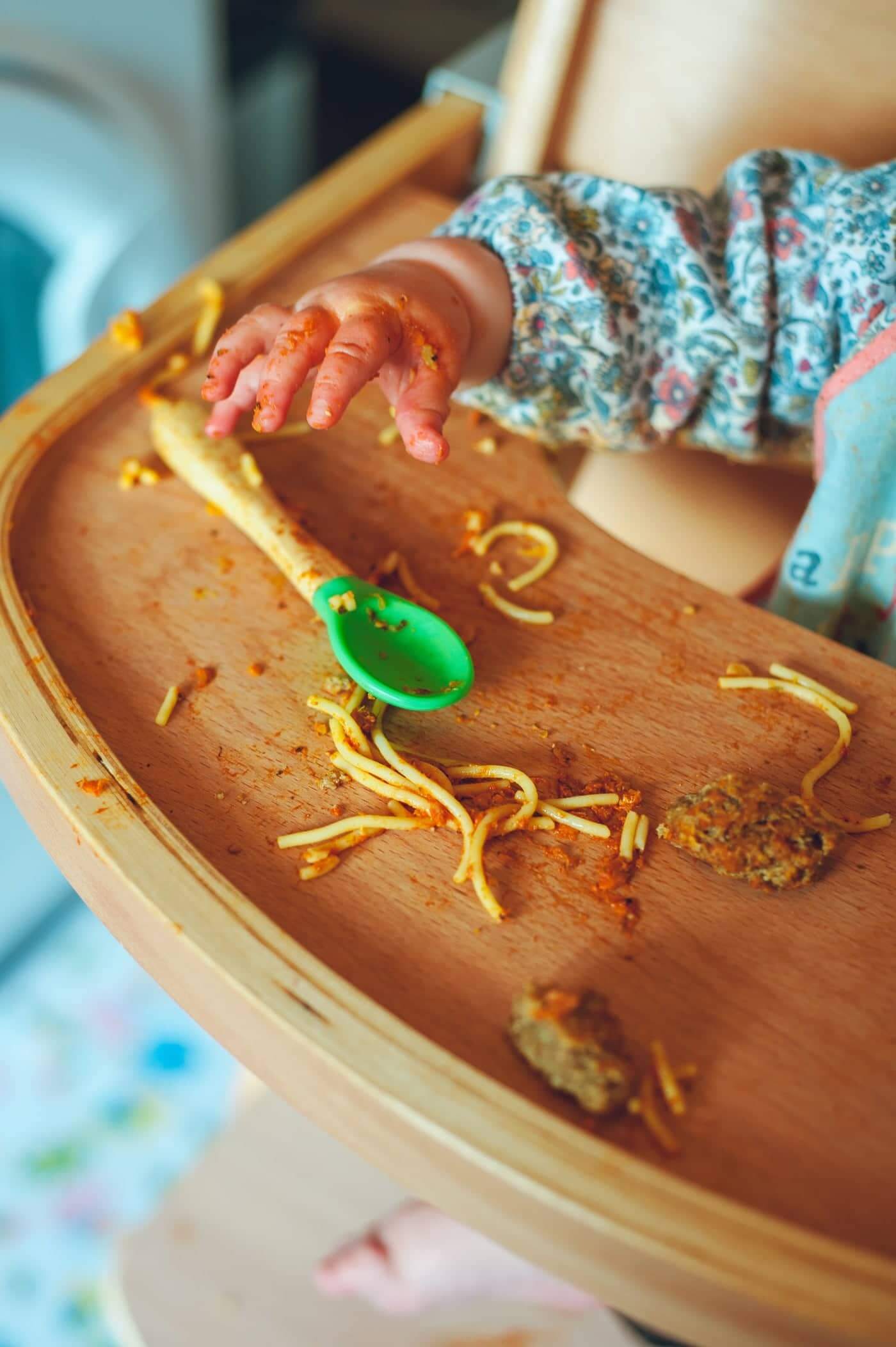 Baby playing with spaghetti and meatballs in a solid wood high chair