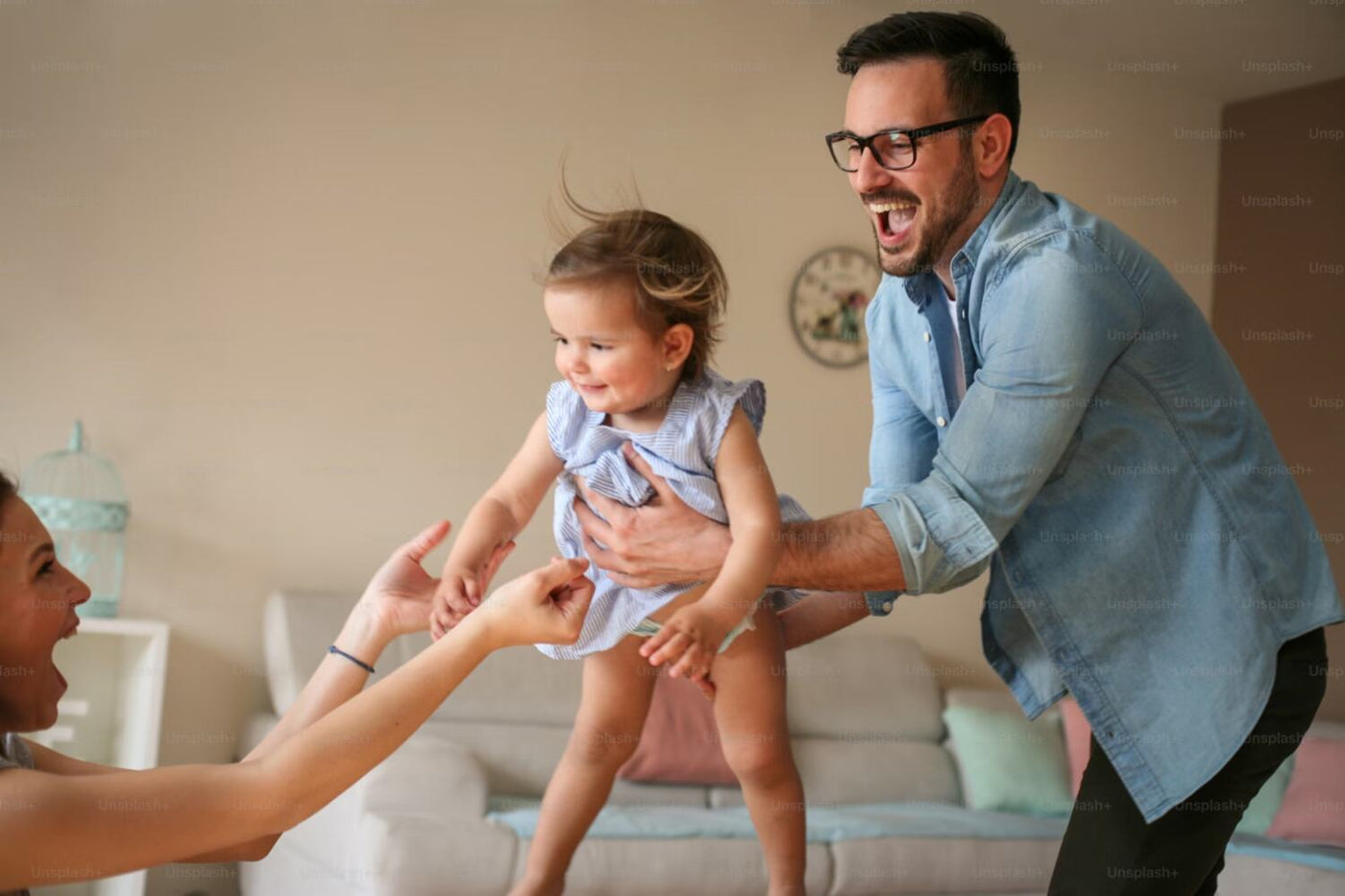 Dad hands toddler to her mom in the living room